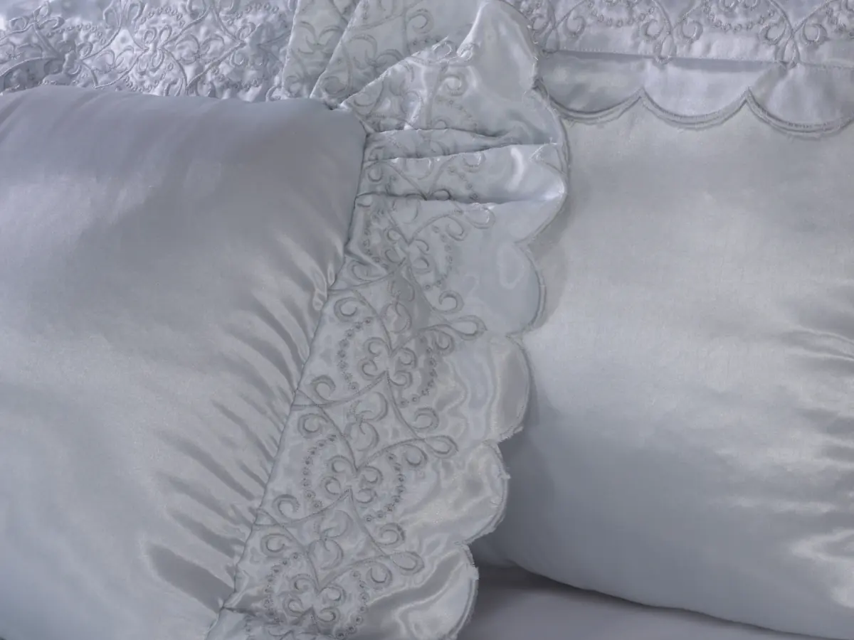 Detalhe do bordado em cetim branco de um kit de cama, com o babado recortado